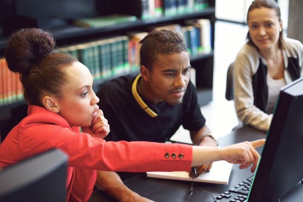 A group of people sitting around a table with laptops.